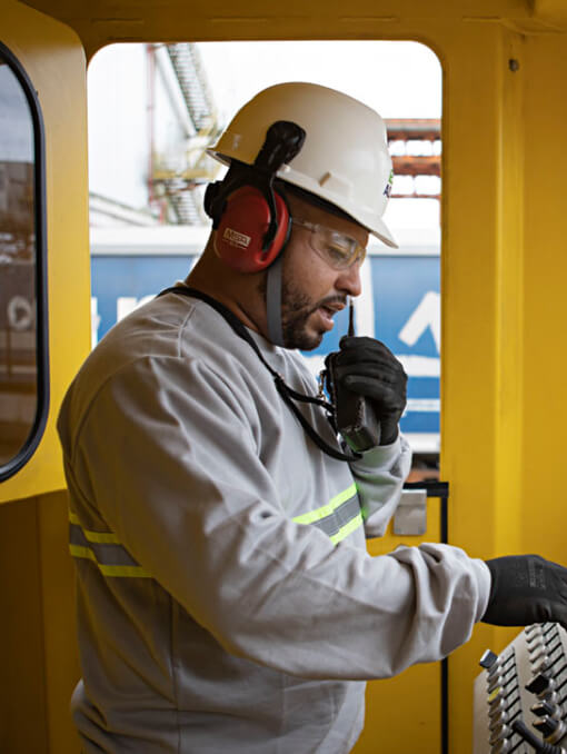 A person in a hardhat operating a train while holding a walkie talkie
