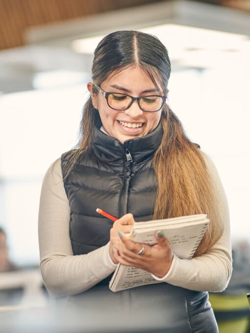 A smiling person writing in a notebook