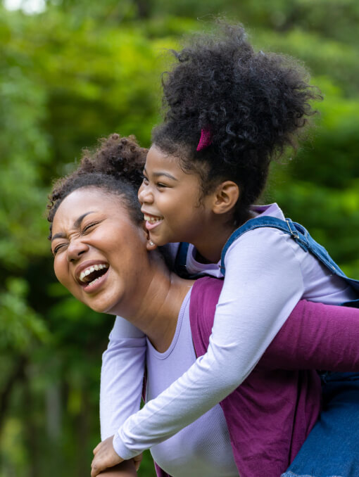 A person smiling while giving a piggyback ride to a child