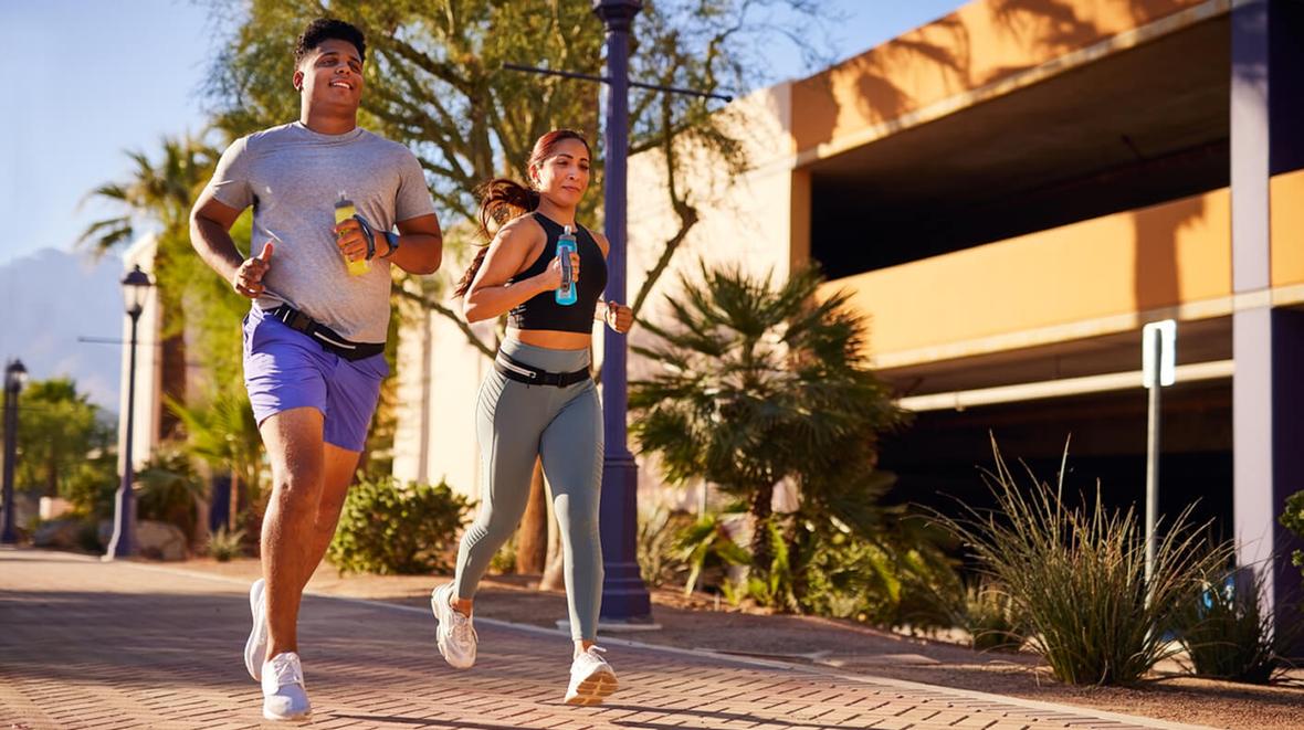Two people jogging on a sidewalk and holding sports drinks
