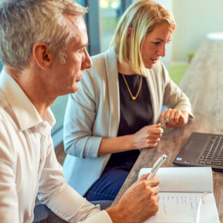 Two people taking notes and looking at a laptop in an office
