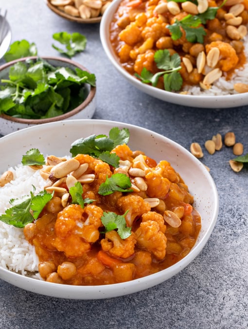 A bowl of rice covered in an orange sauce with chickpeas, peanuts, cauliflower, and other ingredients