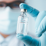 A person wearing gloves holding a vial