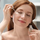 A person applying serum to her face with a dropper