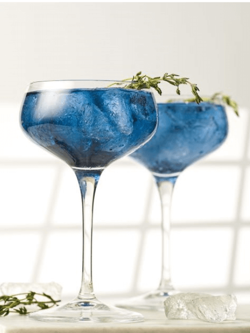 Two dark blue cocktails garnished with sprigs of thyme 