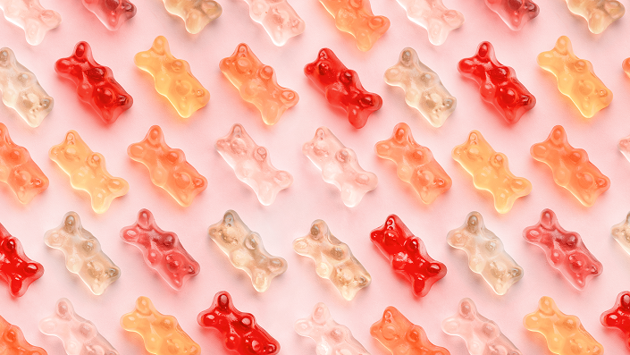 Pink- and red-colored gummy bears lined up on a flat pink surface 