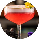 A pink cocktail in a coupe glass and garnished with a yellow pansy
