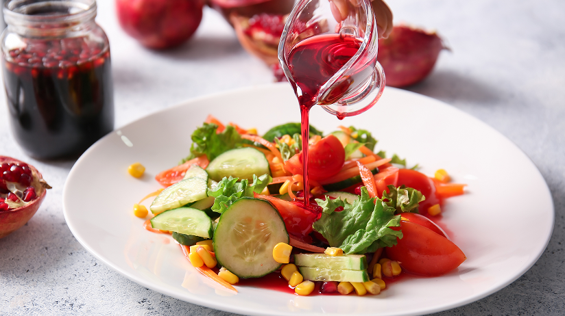 A red dressing being poured onto a fresh vegetable salad