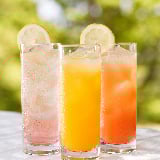 Three glasses containing different fruit juices sit on a table 