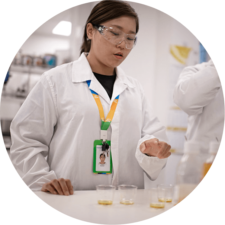 An ADM employee in a lab coat and safety goggles testing liquids in multiple clear cups