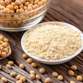 A bowl of soy flour with loose soybeans scattered around it