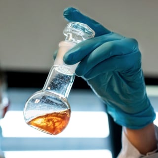 A person’s hand holding up a liquid sample in a glass bottle
