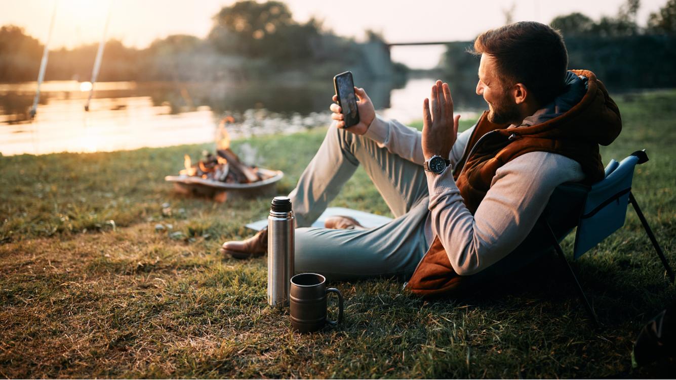 A person sitting on grass by a fire talking on the phone 