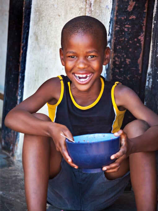 A smiling child sitting on the ground holding a bowl