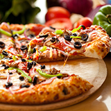 A supreme pizza with black olives, green peppers, and sausage with a slice being lifted from the rest of the pizza